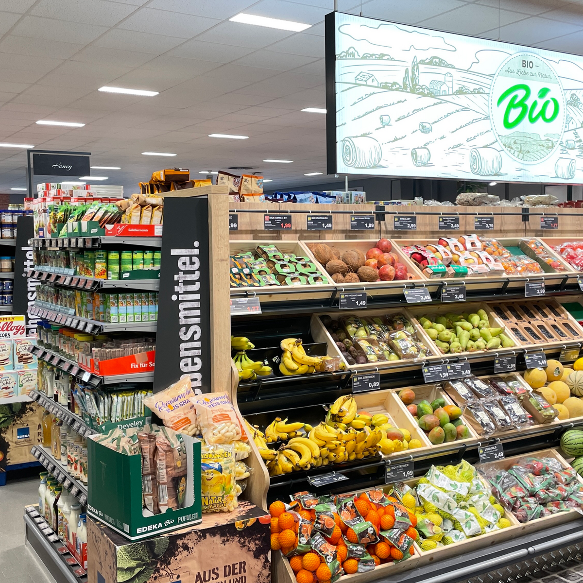 Ein Obstregal im Supermarkt, gefüllt mit verschiedenen Sorten frischem Obst und Preisschildern.